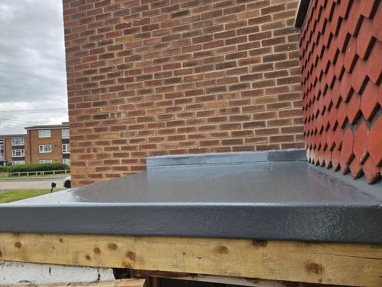 Close-up of a GRP edge trim and upstand where a flat roof meets a brick wall and tiled roof