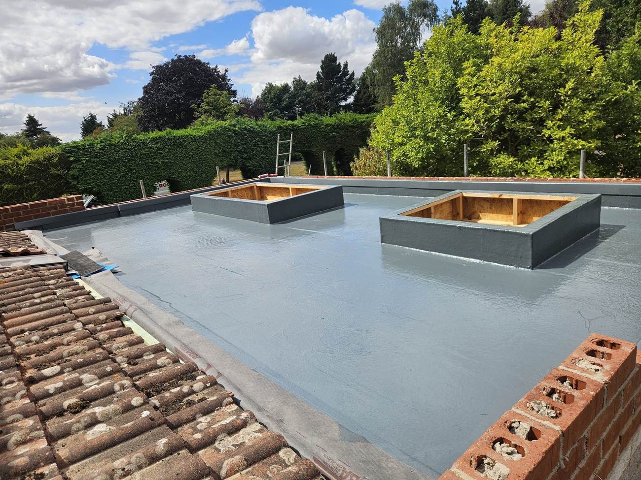 Freshly laid grey GRP flat roof with two new rooflight kerbs on a house extension