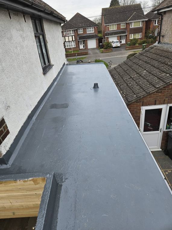 Dark grey GRP roof on a house extension with a vent pipe and an upstand against a rendered wall